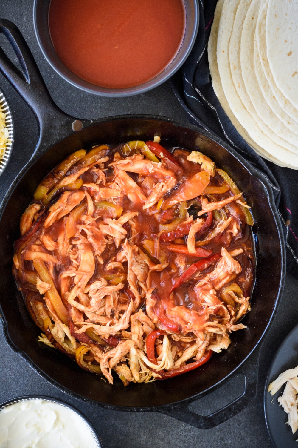 A black cast iron skillet with sliced bell peppers, shredded chicken, and enchilada sauce in the skillet.