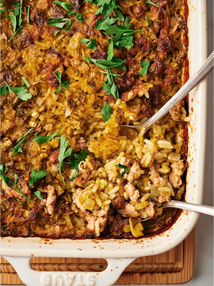 A baking dish filled with freshly baked sausage and rice casserole with two spoons in the casserole dish and fresh parsley on top.