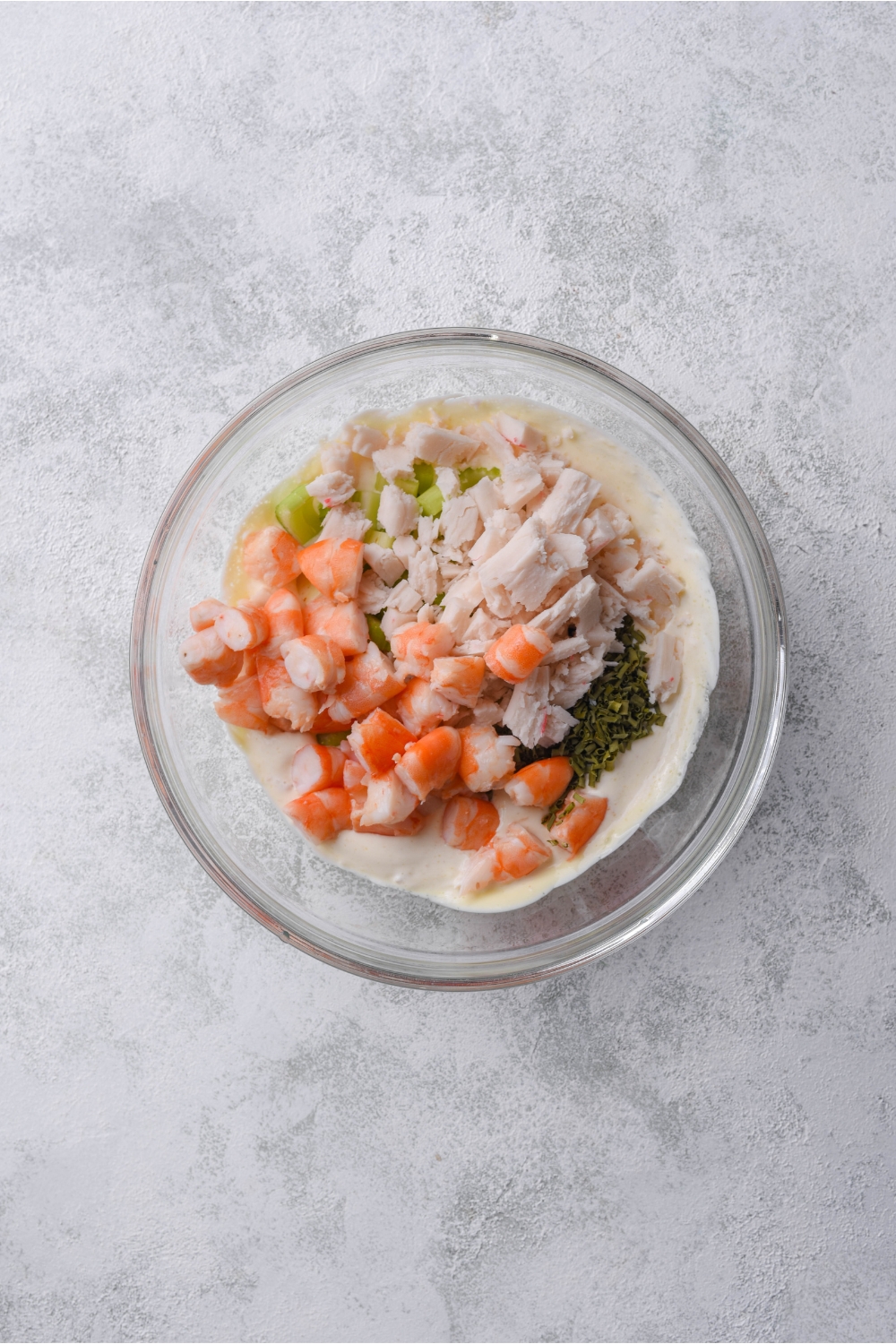 A clear bowl filled with crab meat, shrimp chunks, diced celery, and herbs in a creamy dressing.