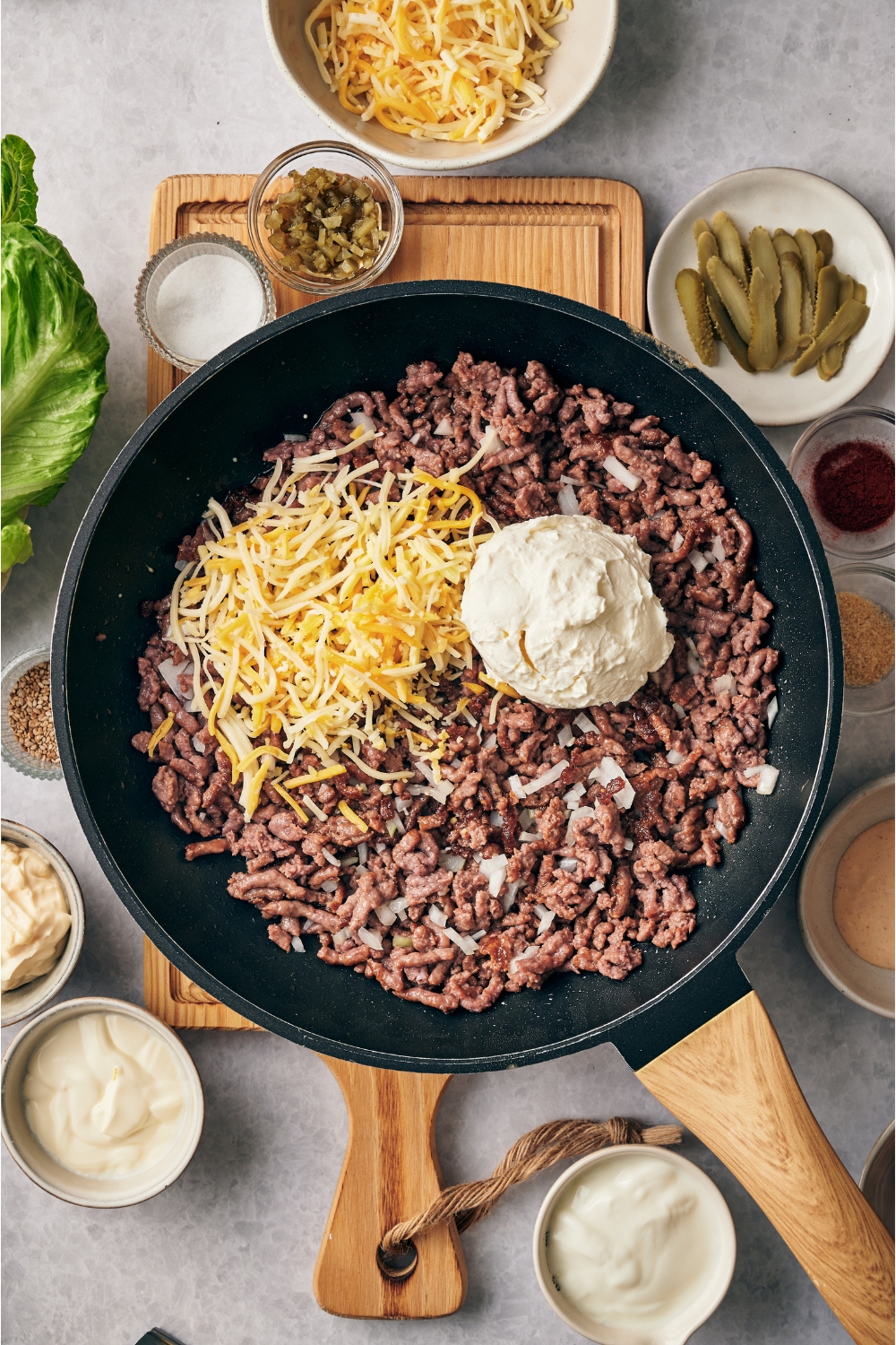 Skillet filled with cooked ground beef, diced onion, a scoop of cream cheese, and a pile of shredded cheese.