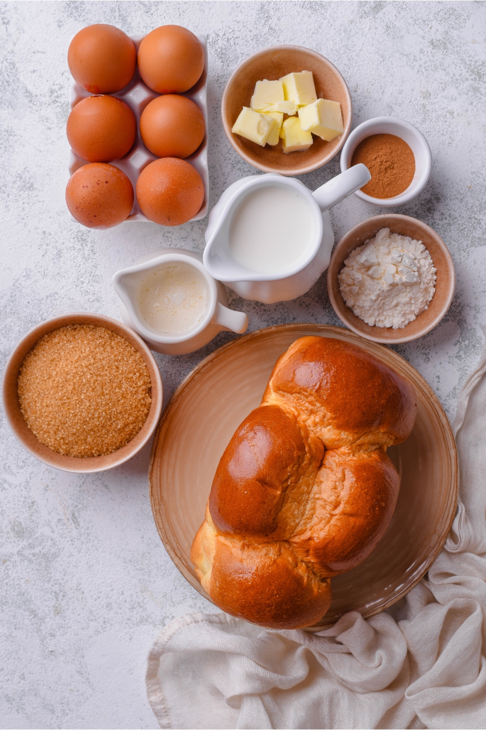 A countertop with brioche bread, brown sugar, milk, flour, cinnamon, butter, egg, and heavy cream.