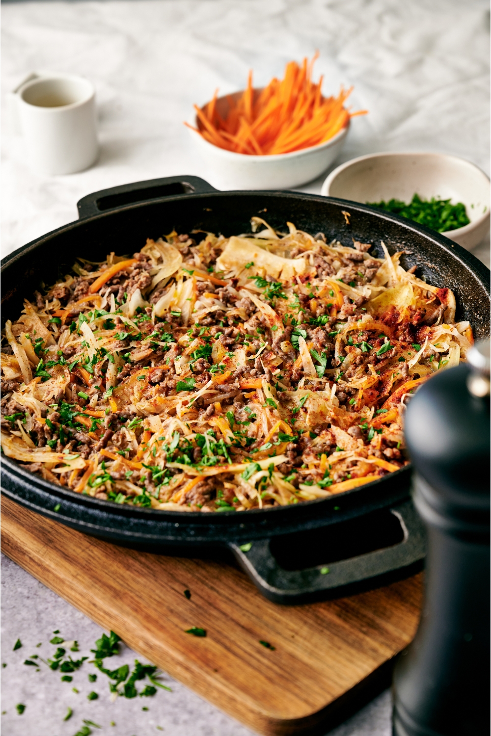 A black skillet filled with ground beef and cabbage stir fry garnished with fresh parsley. The skillet is on a wooden board.