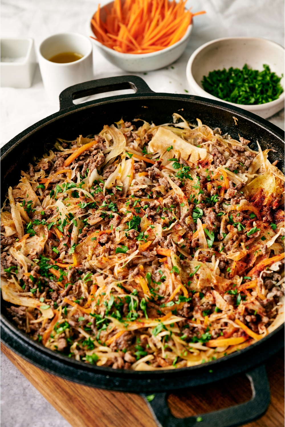 A black skillet filled with ground beef and cabbage stir fry garnished with fresh parsley. The skillet is on a wooden board.