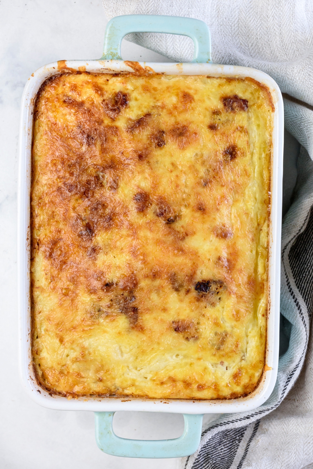 A baking dish filled with a freshly baked casserole covered in a golden brown layer of melted cheese.