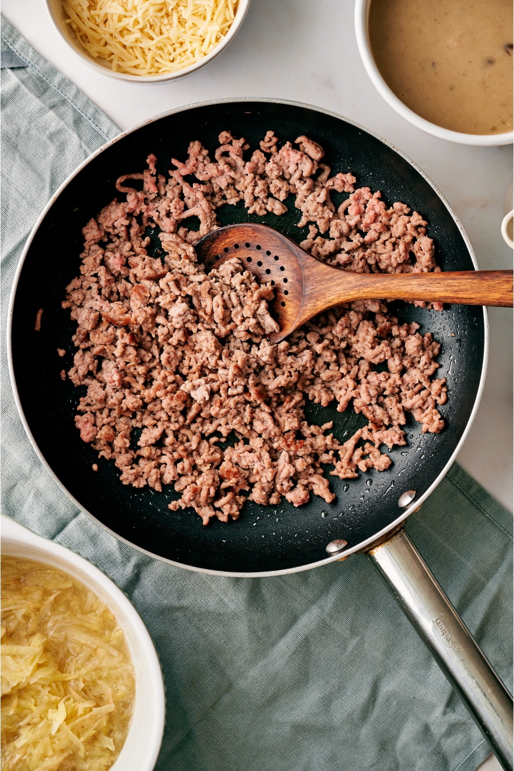 A black nonstick skillet filled with brown beef being stirred using a wooden spoon.