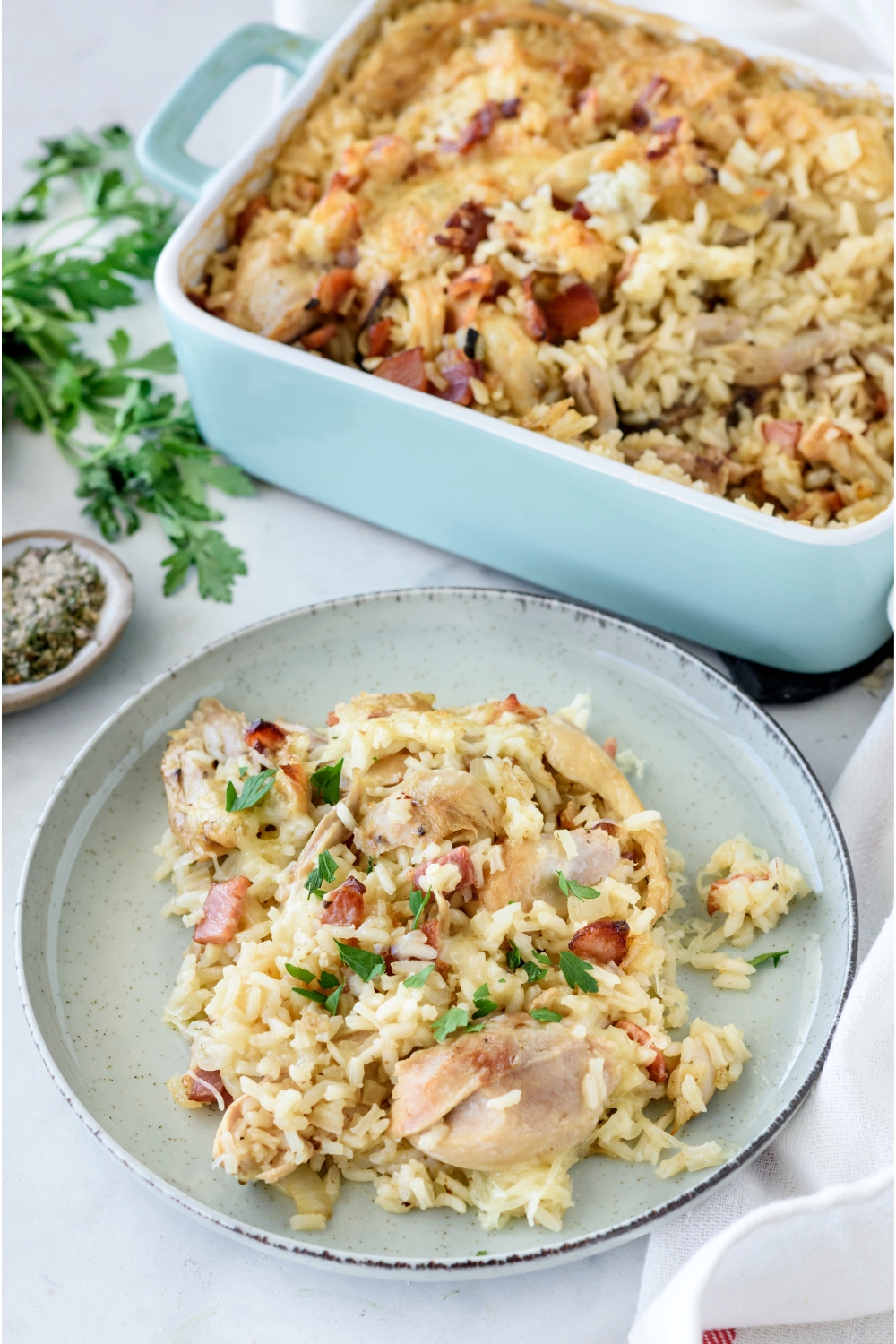 A heaping plate of chicken bacon and rice casserole garnished with fresh green herbs next to a baking dish filled with the remainder of the casserole.