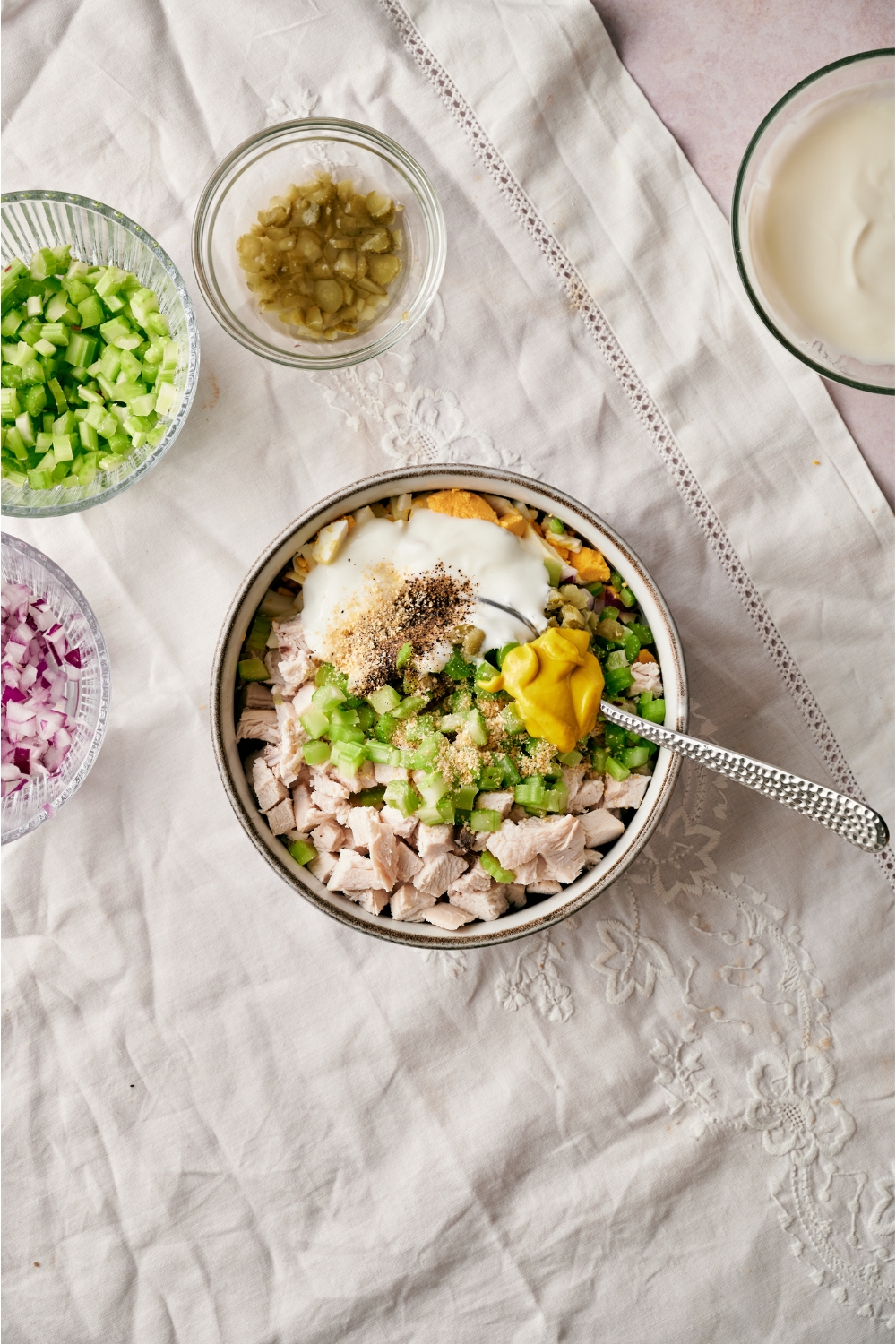 A bowl of cubed chicken with diced celery, chopped hard boiled eggs, mayonnaise, yellow mustard, and spices, with a spoon in the bowl.