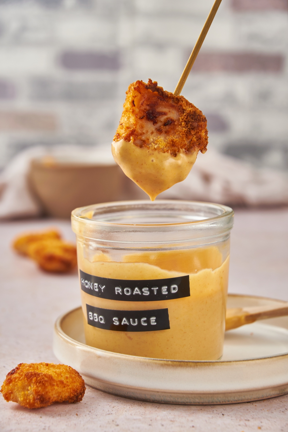 A nugget held by a toothpick being dipped in a jar labeled "honey roasted bbq sauce."