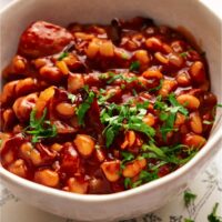 A bowl of baked beans in a brown sauce with fresh green herbs on top.