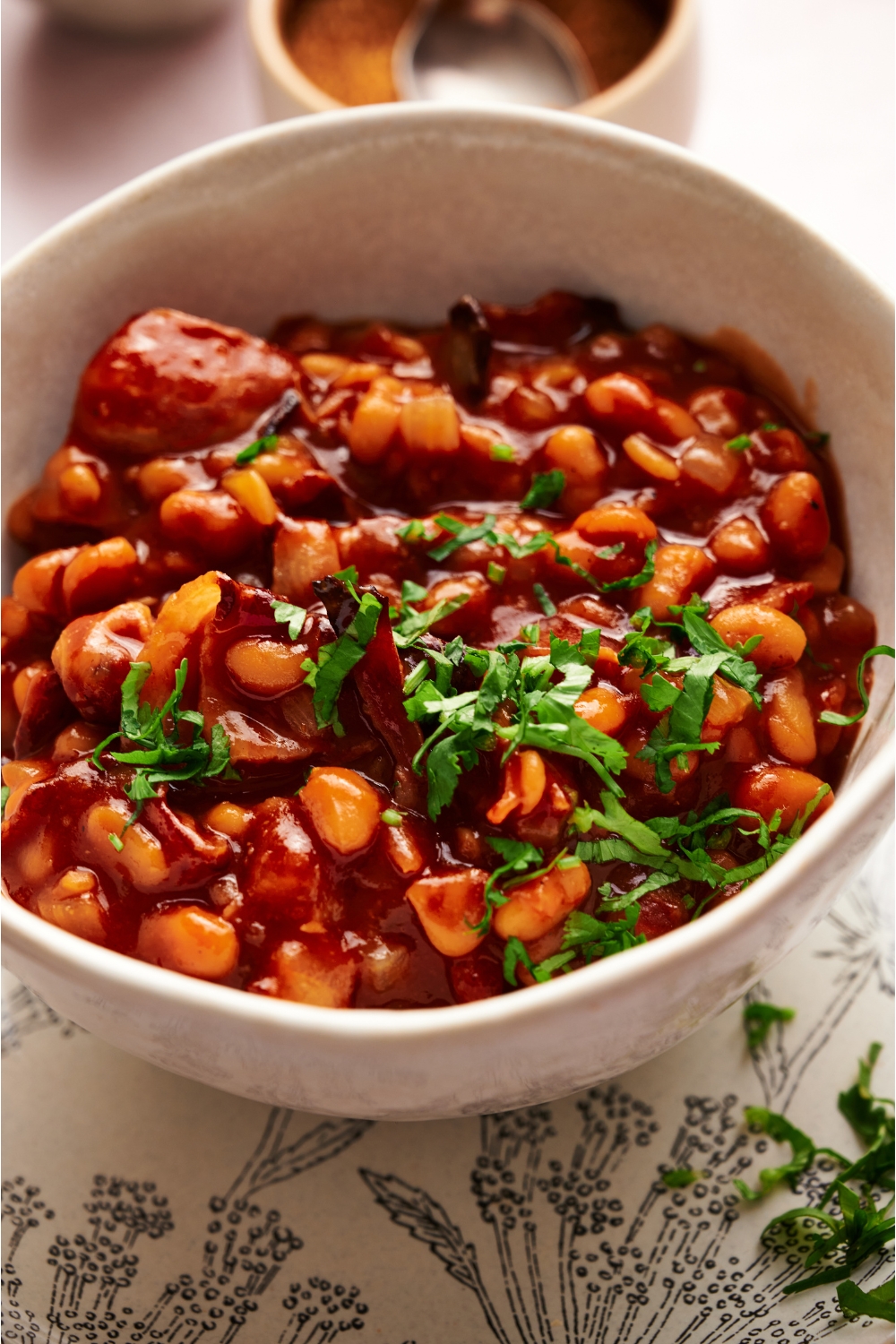 A bowl of baked beans in a brown sauce with fresh green herbs on top.