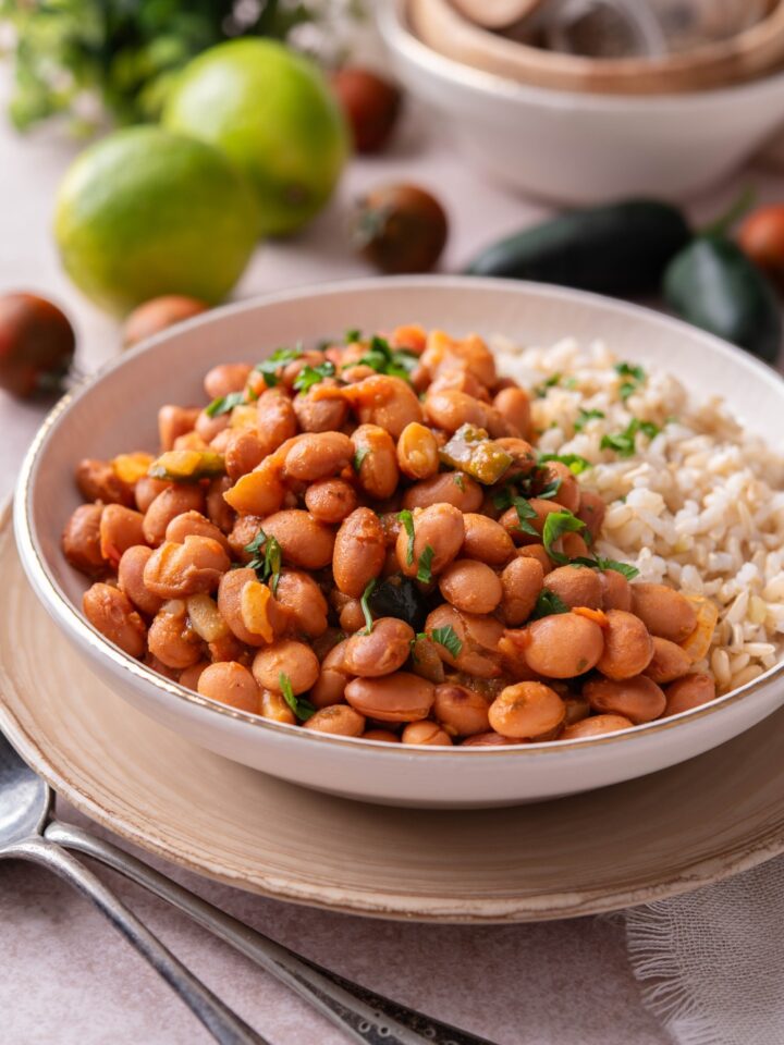 A bowl of Mexican pinto beans with a side of brown rice and fresh green herbs on top.