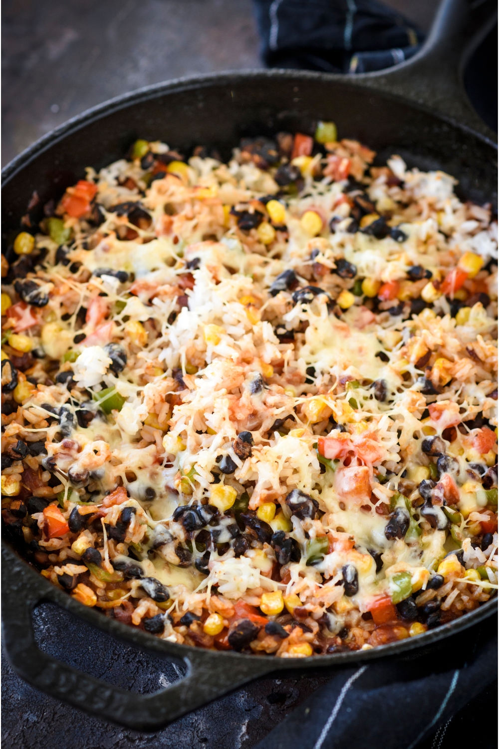 A skillet filled with rice casserole covered in melted cheese with black beans, corn, and diced peppers in it.