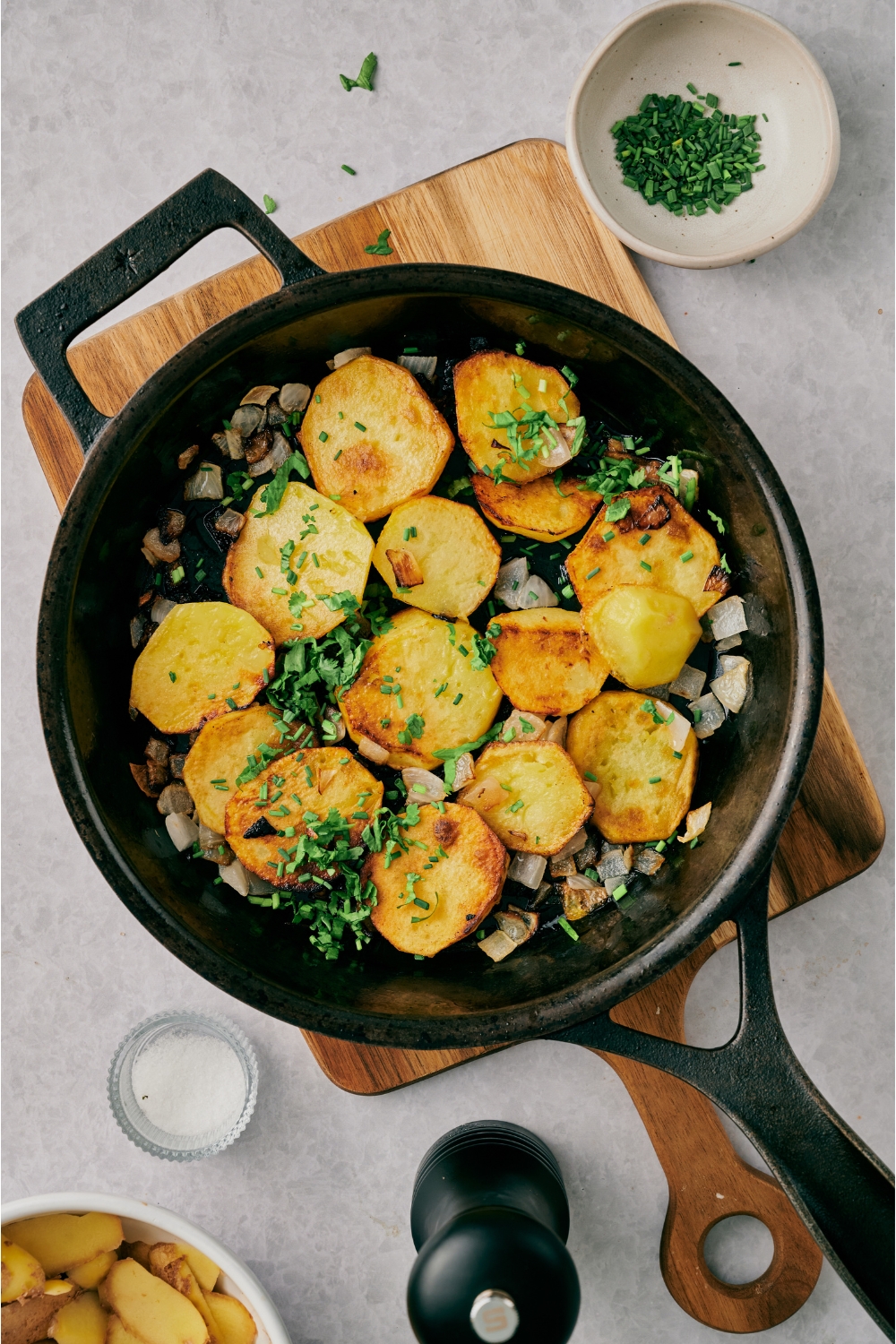 A skillet with pan fried potatoes and onions garnished with fresh green herbs.