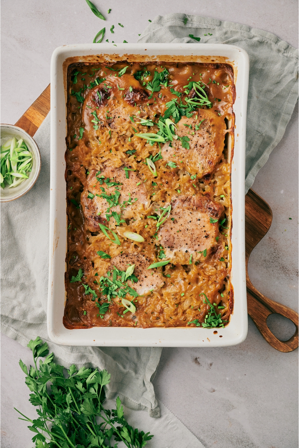 A baking dish filled with freshly baked pork chops and rice in a seasoned cream sauce with green onions on top.