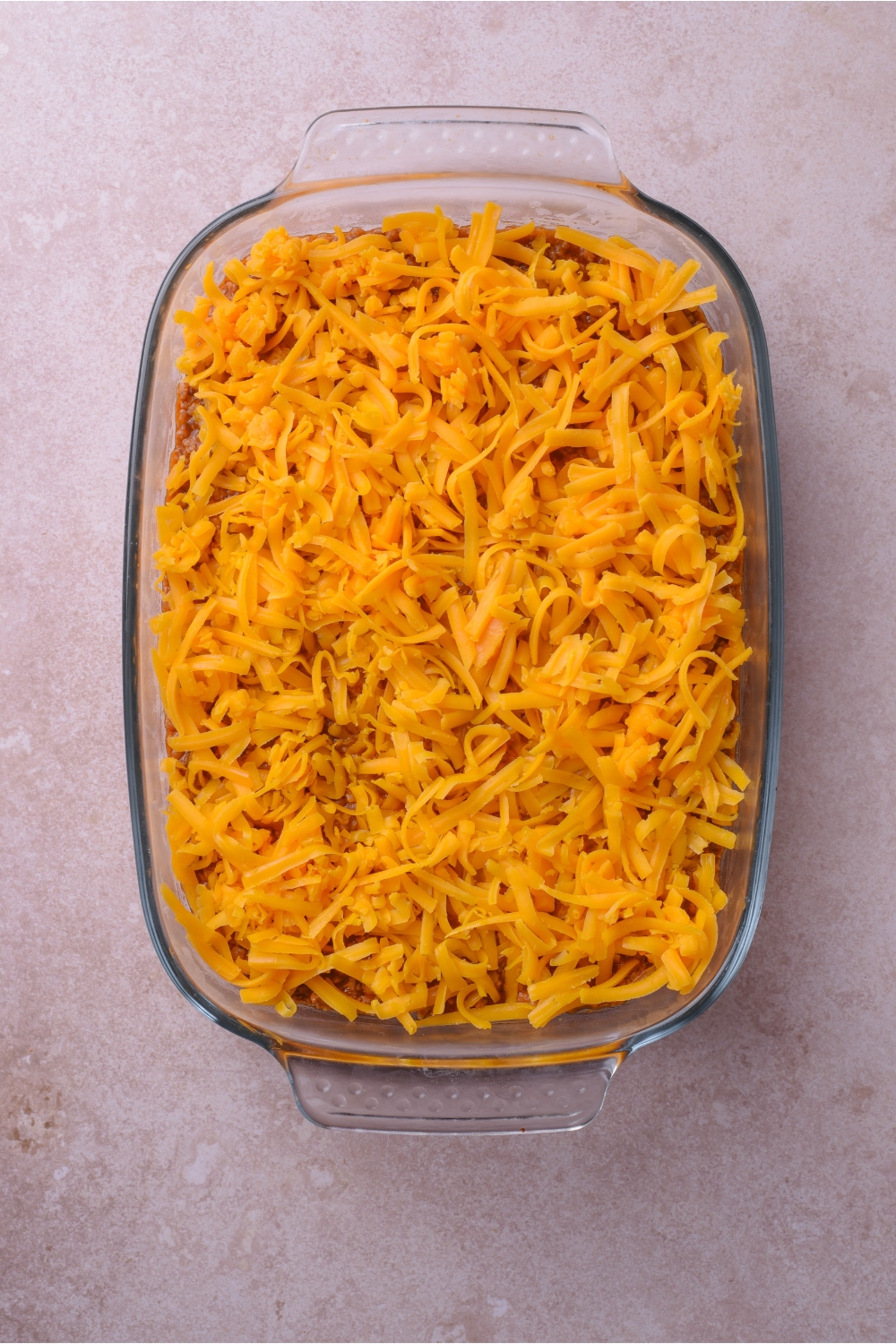A clear baking dish filled with an unbaked casserole covered in shredded cheese.
