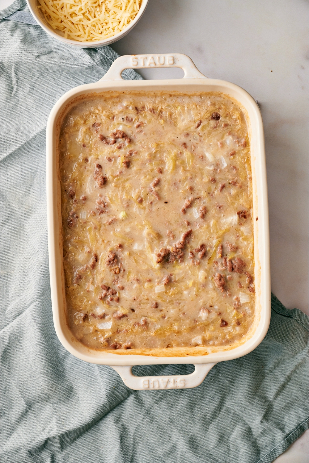 A white baking dish filled with unbaked ground beef and hashbrown casserole.