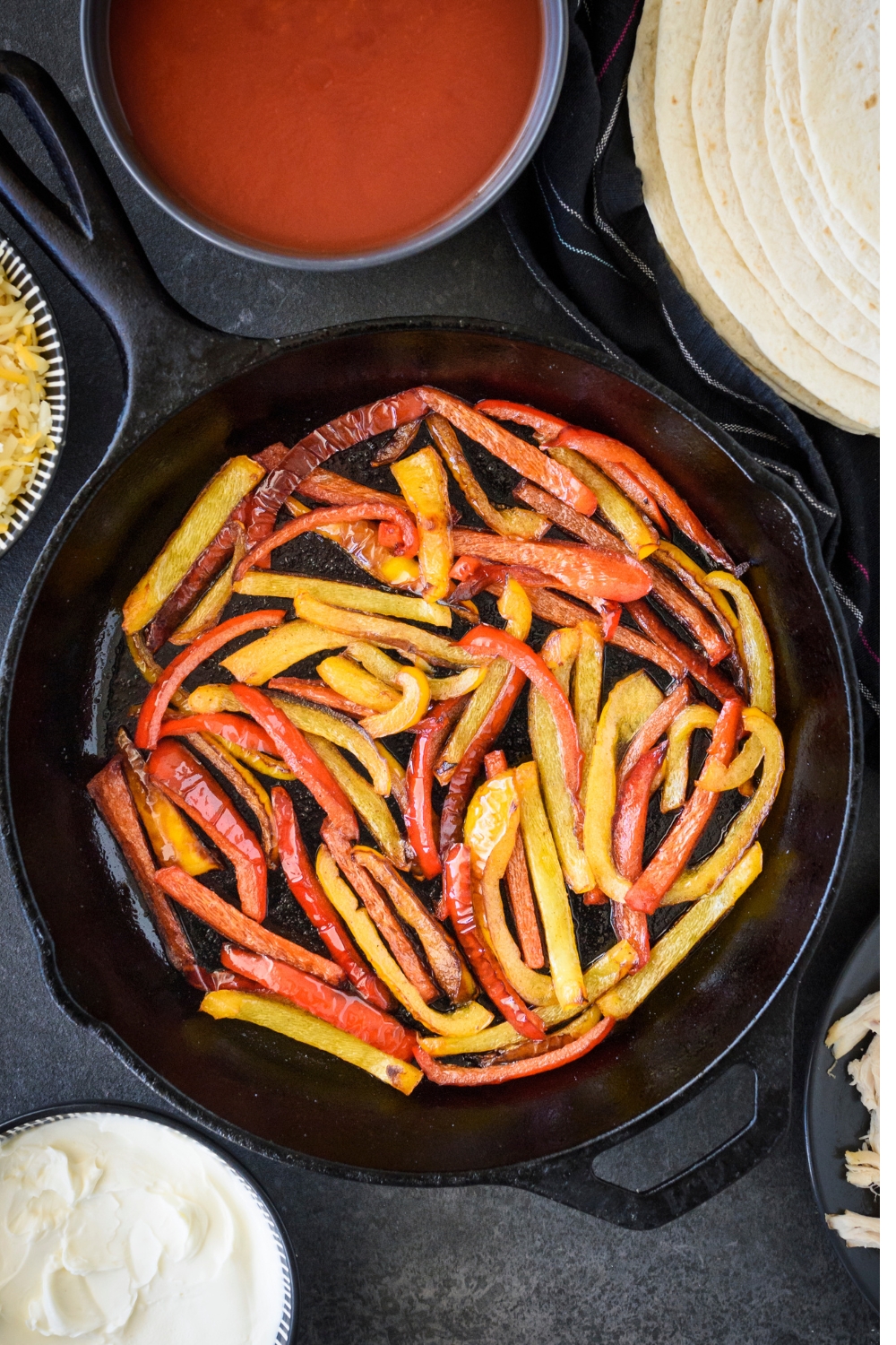 A black cast iron skillet filled with yellow and red bell peppers being sautéed.