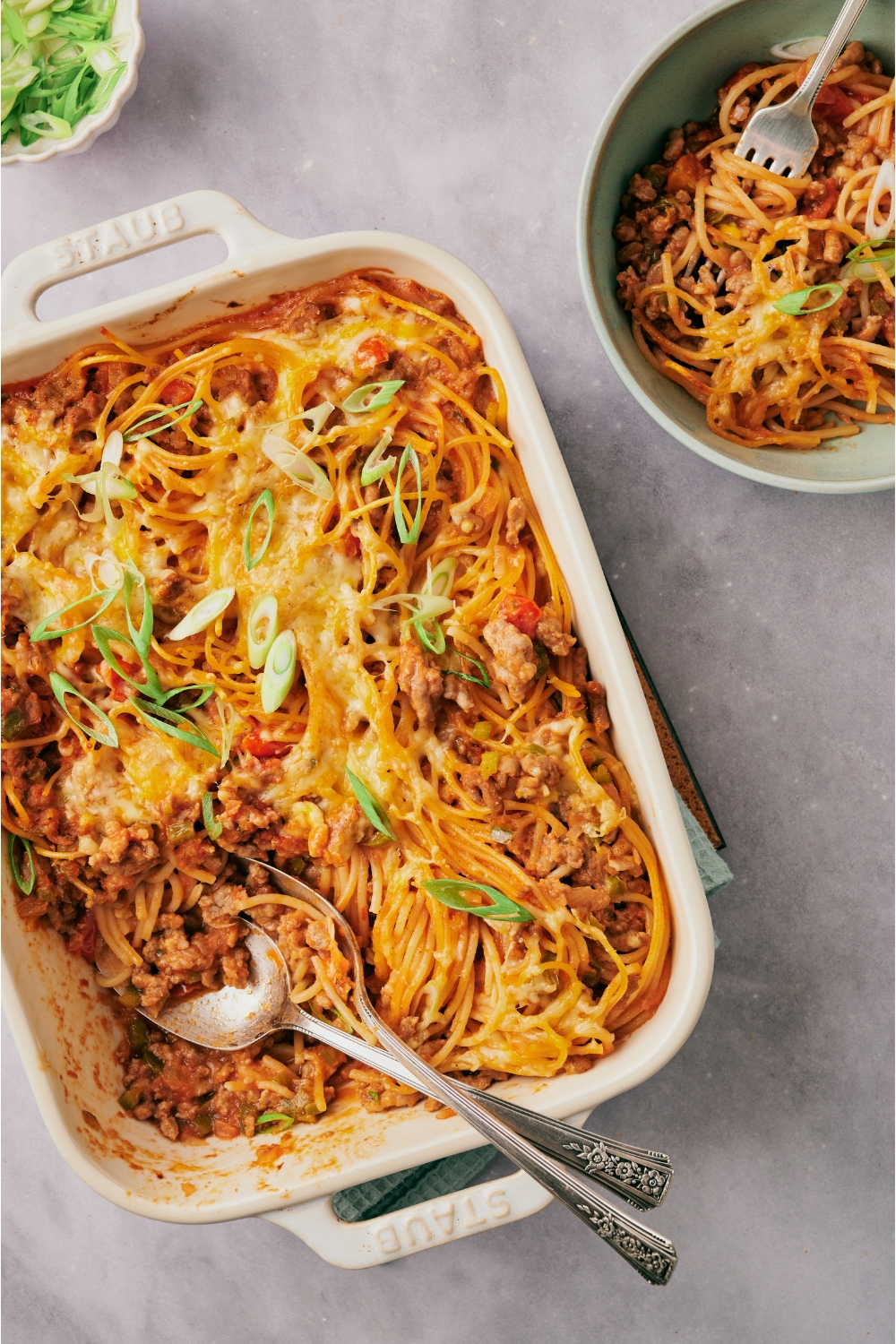 A baking dish filled with cooked Mexican spaghetti. A serving has been scooped out and added to a bowl next to the baking dish.