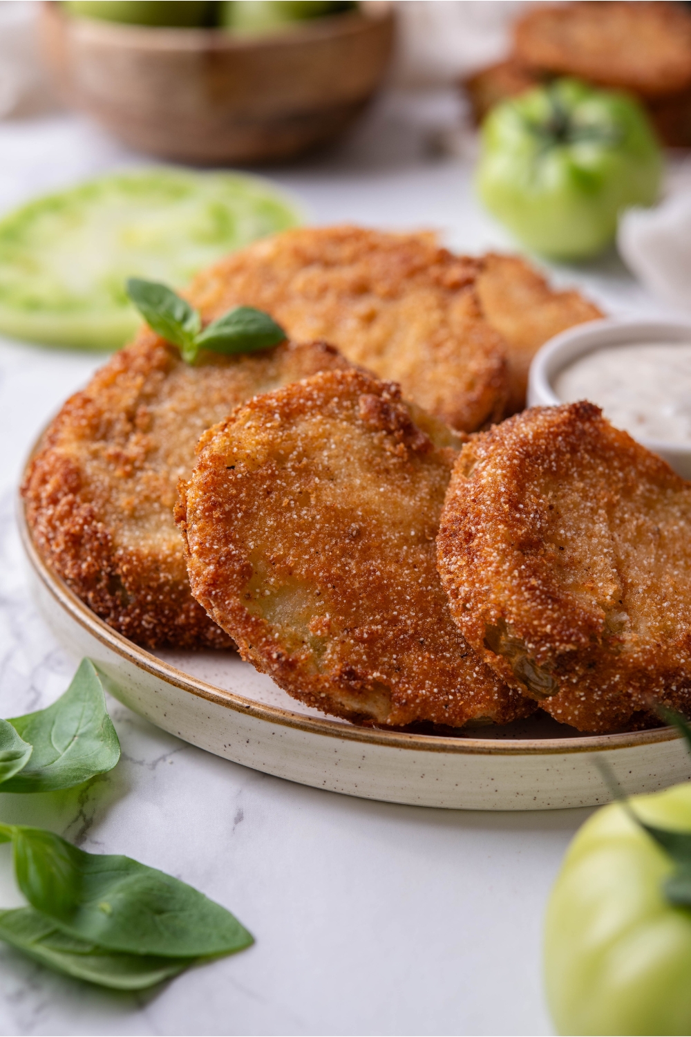 Three slices of breaded and fried green tomatoes overlapping each other on a plate with a small bowl of dipping sauce and a garnish of green herbs.