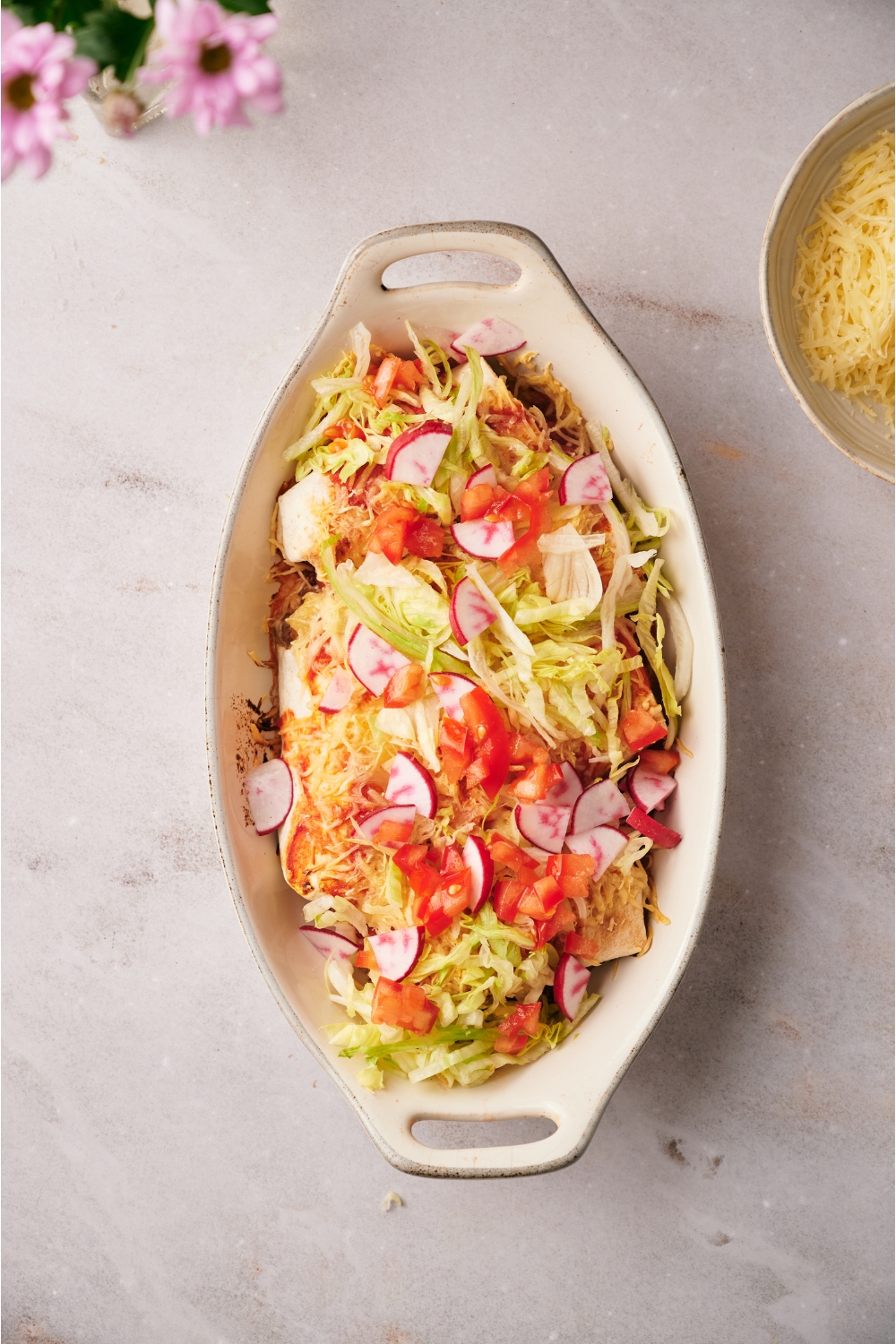 A baking dish filled with freshly baked casserole covered in diced tomato, sliced radishes, and shredded lettuce.