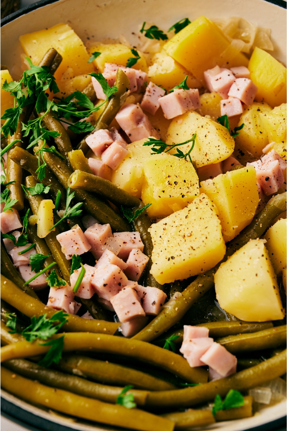 A close up of ham, green beans, and potatoes with seasonings and parsley garnish on top.