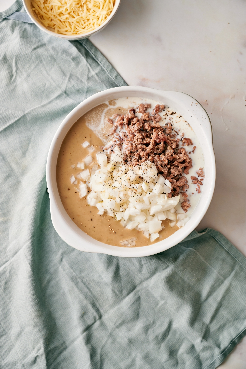 A white mixing bowl filled with cooked ground beef, diced onion, milk, and cream of mushroom soup added but not combined.