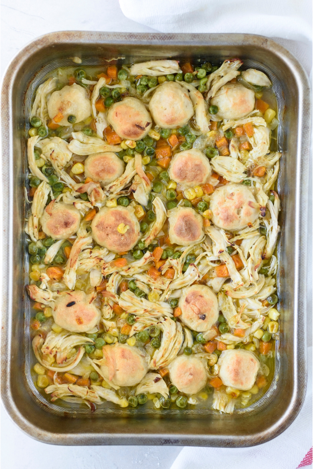 A baking dish filled with freshly baked and shredded chicken mixed with cooked veggies and dumplings on top.