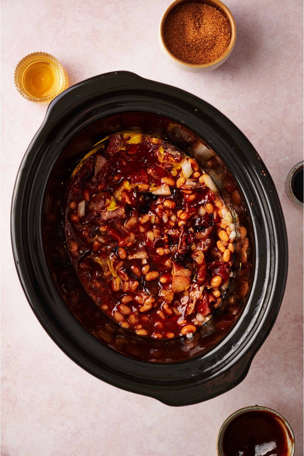 A crock pot filled with canned beans mixed with diced onion and a brown sauce mixture.