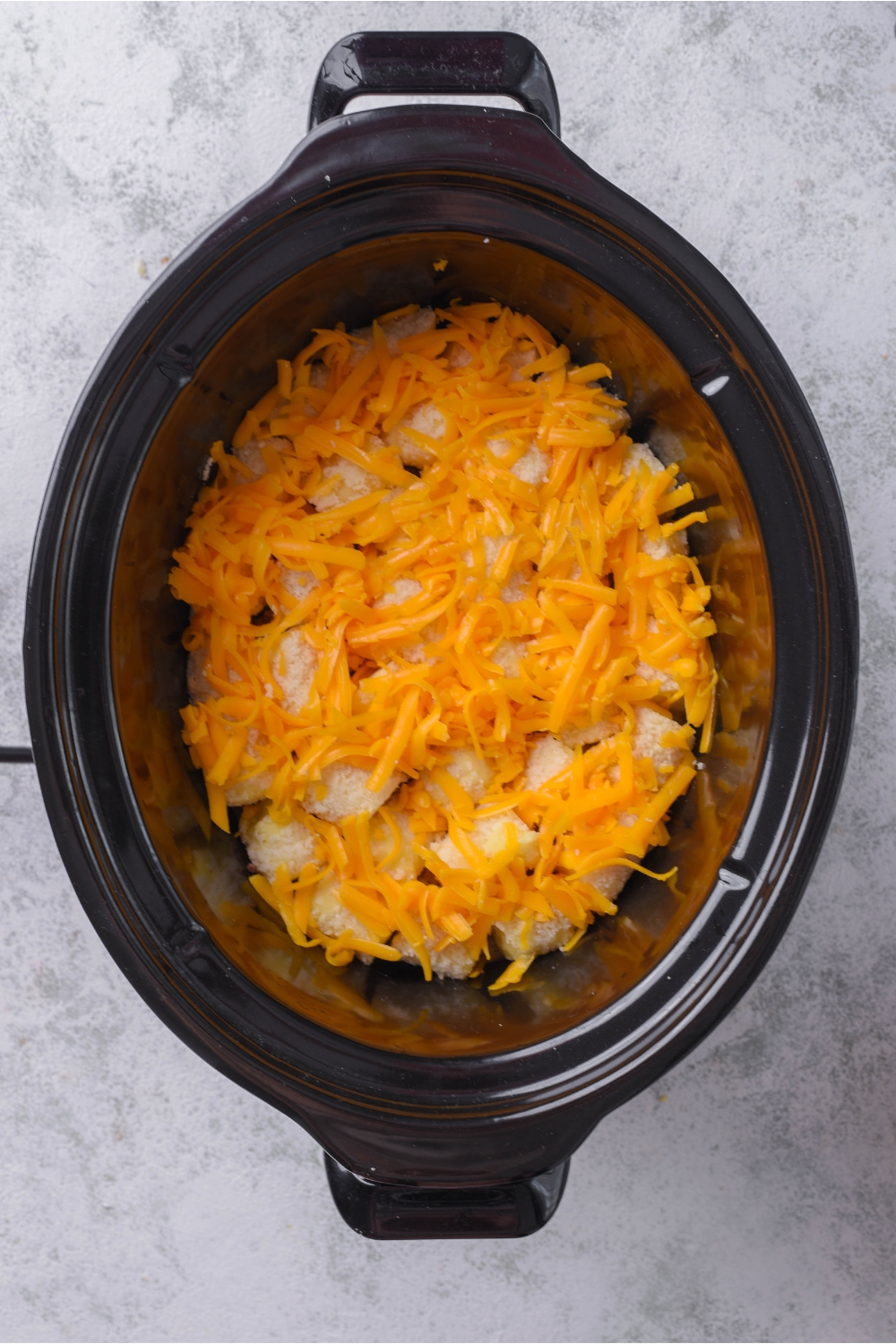 A slow cooker filled with tater tots and a layer of shredded cheese on top of the tater tots.