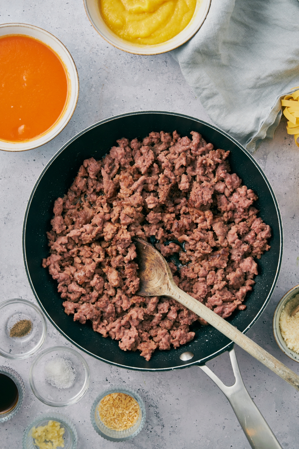 A skillet filled with cooked ground beef broken up using a wooden spoon.