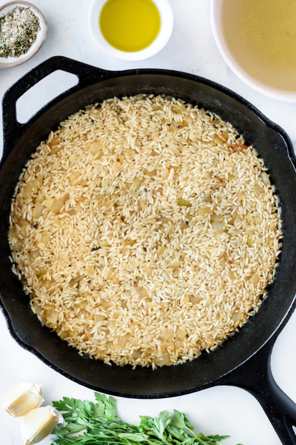 A black skillet filled with dried rice and diced onion simmering in liquid.