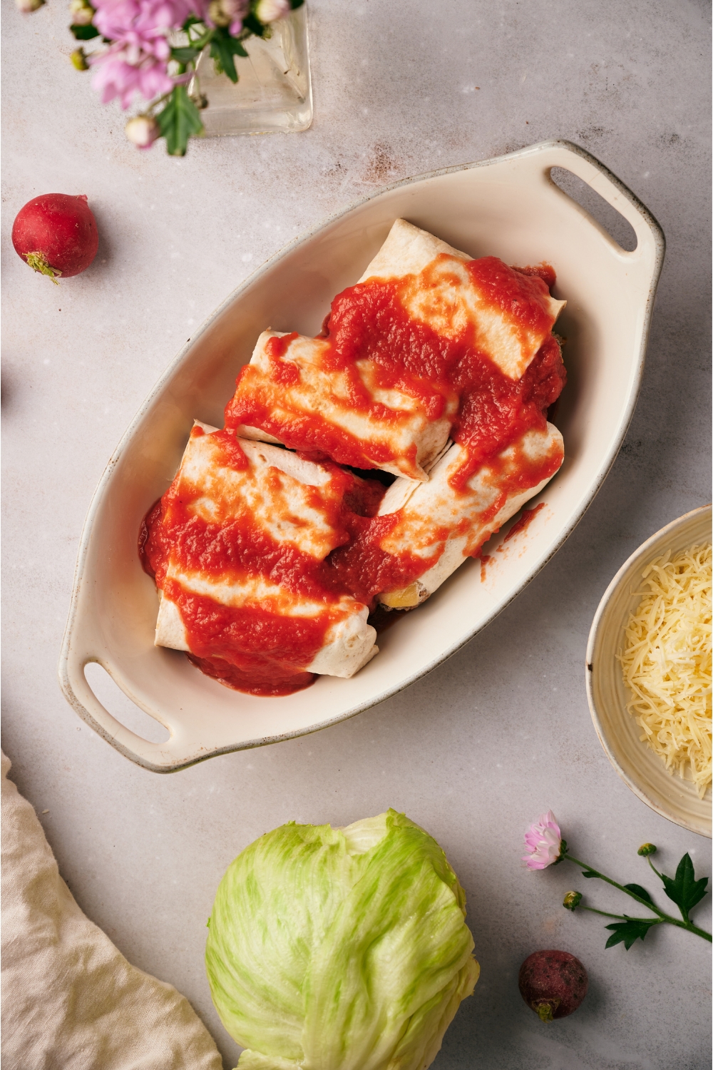 A baking dish filled with five mini burritos covered in a layer of red sauce.