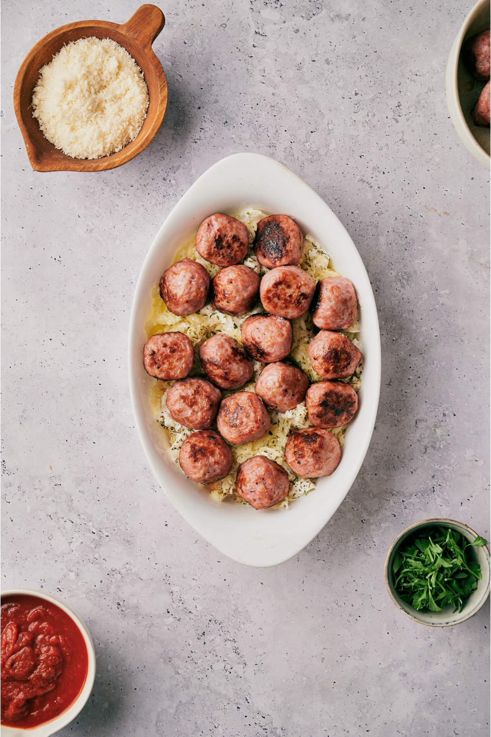 An oval baking dish filled with browned meatballs atop a layer of cream cheese.