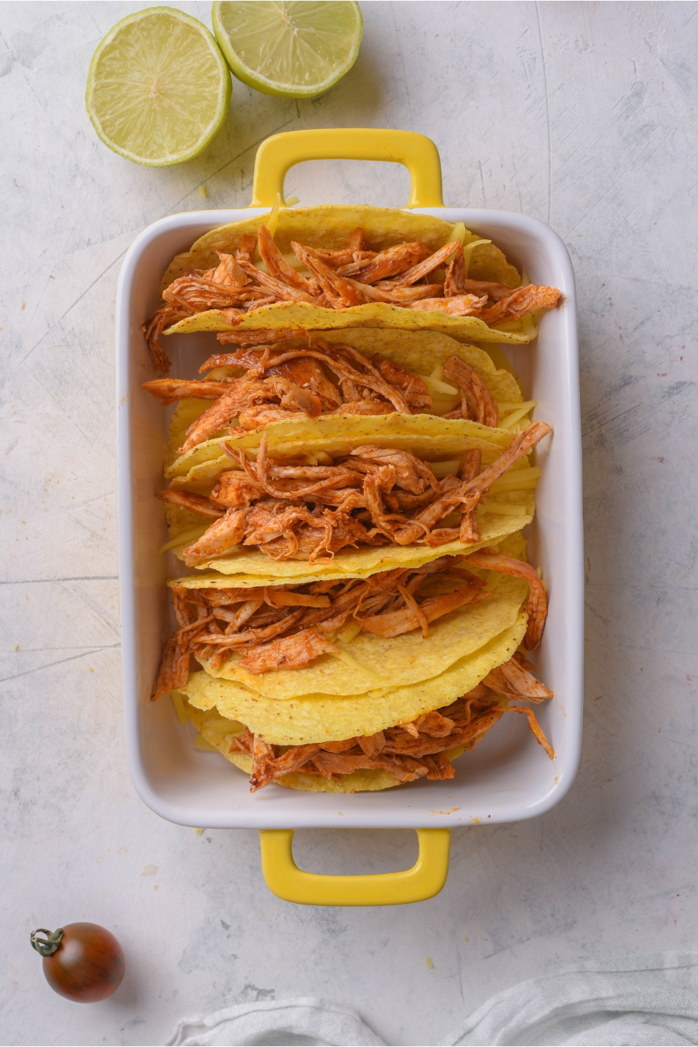 Five hard taco shells filled with seasoned shredded chicken in a baking dish.