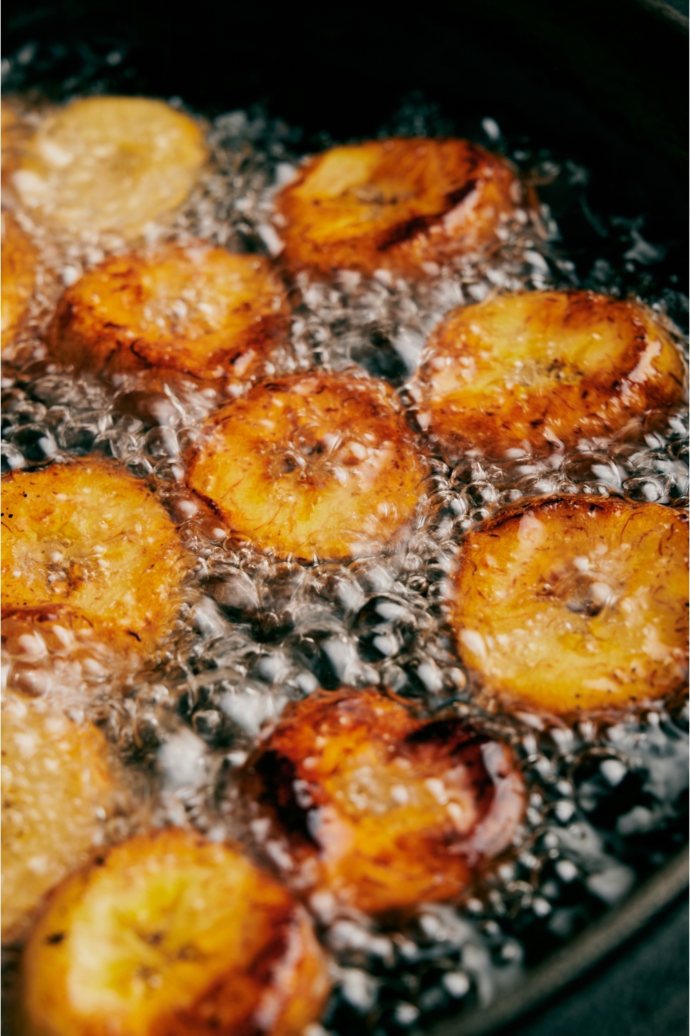 Close up of golden brown plantain slices frying in bubbling oil.