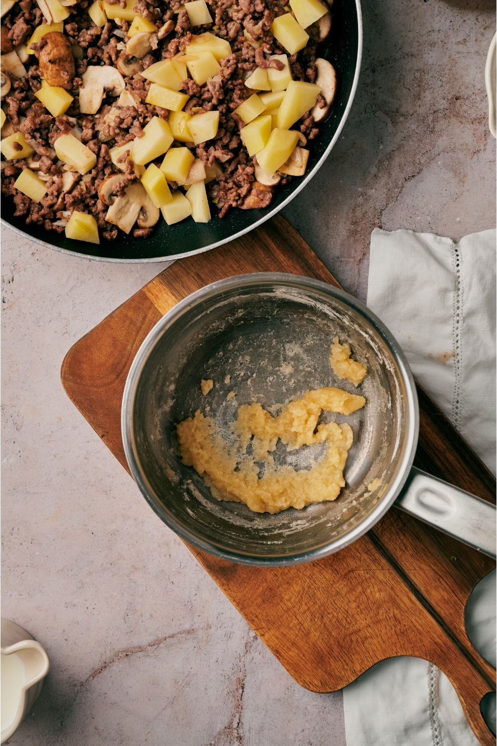 A small pot on a wooden board with a roux mixture in it.