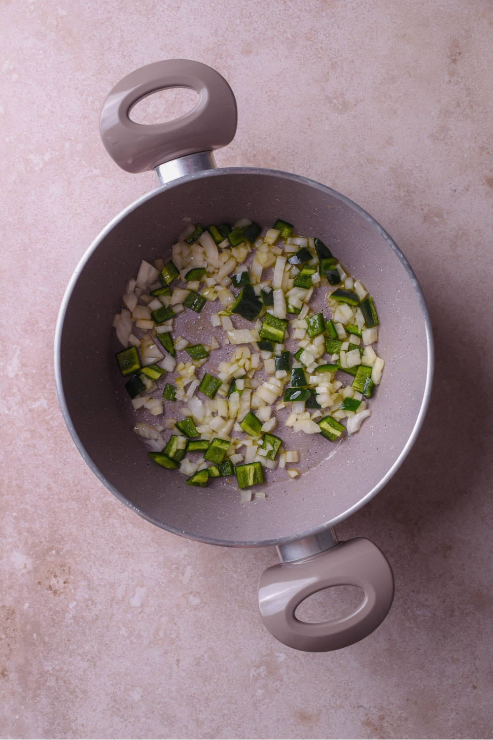 A large pot with diced green peppers and diced onion cooking in the pot.