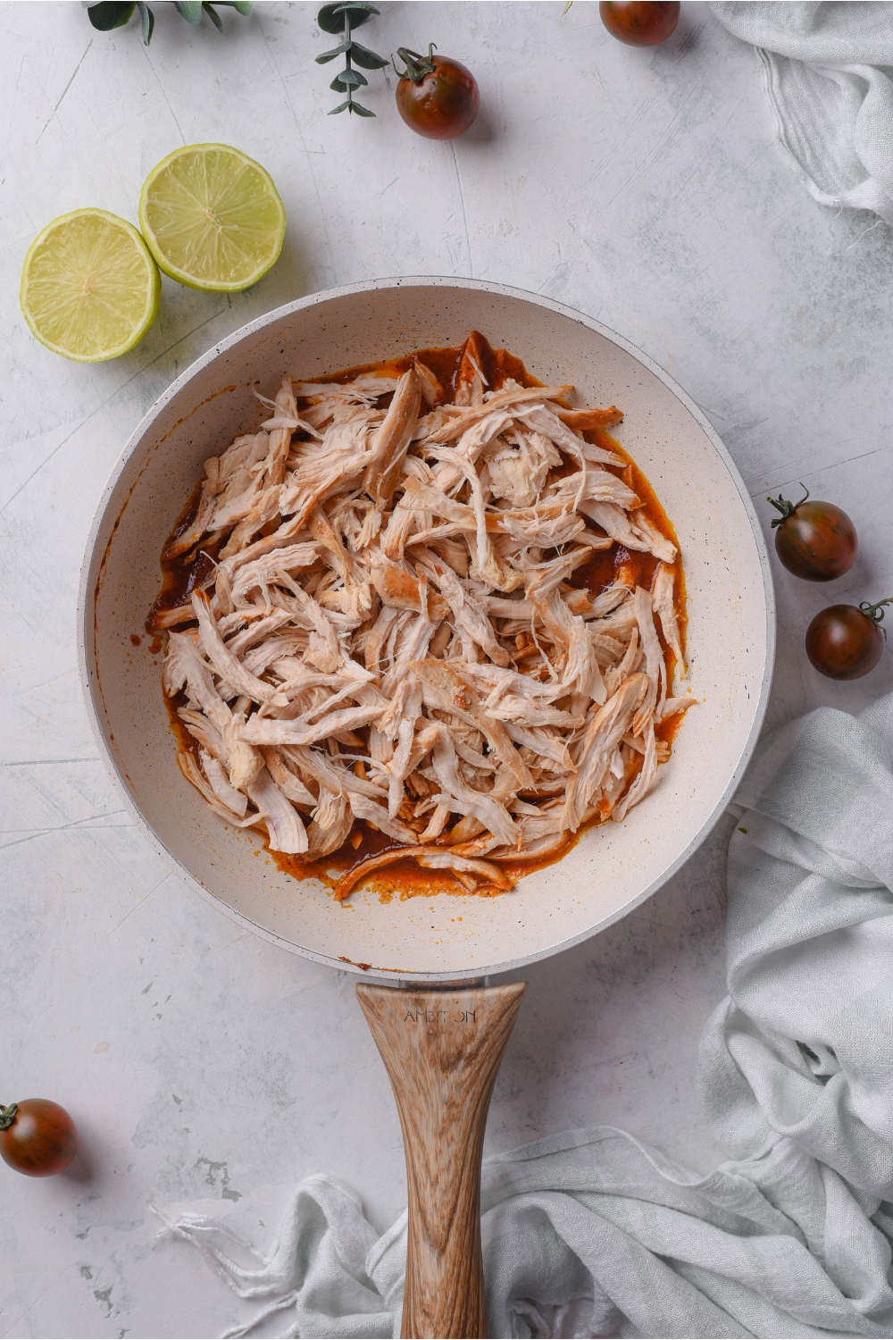 A skillet with cooked and shredded chicken atop a seasoned sauce but not yet combined.