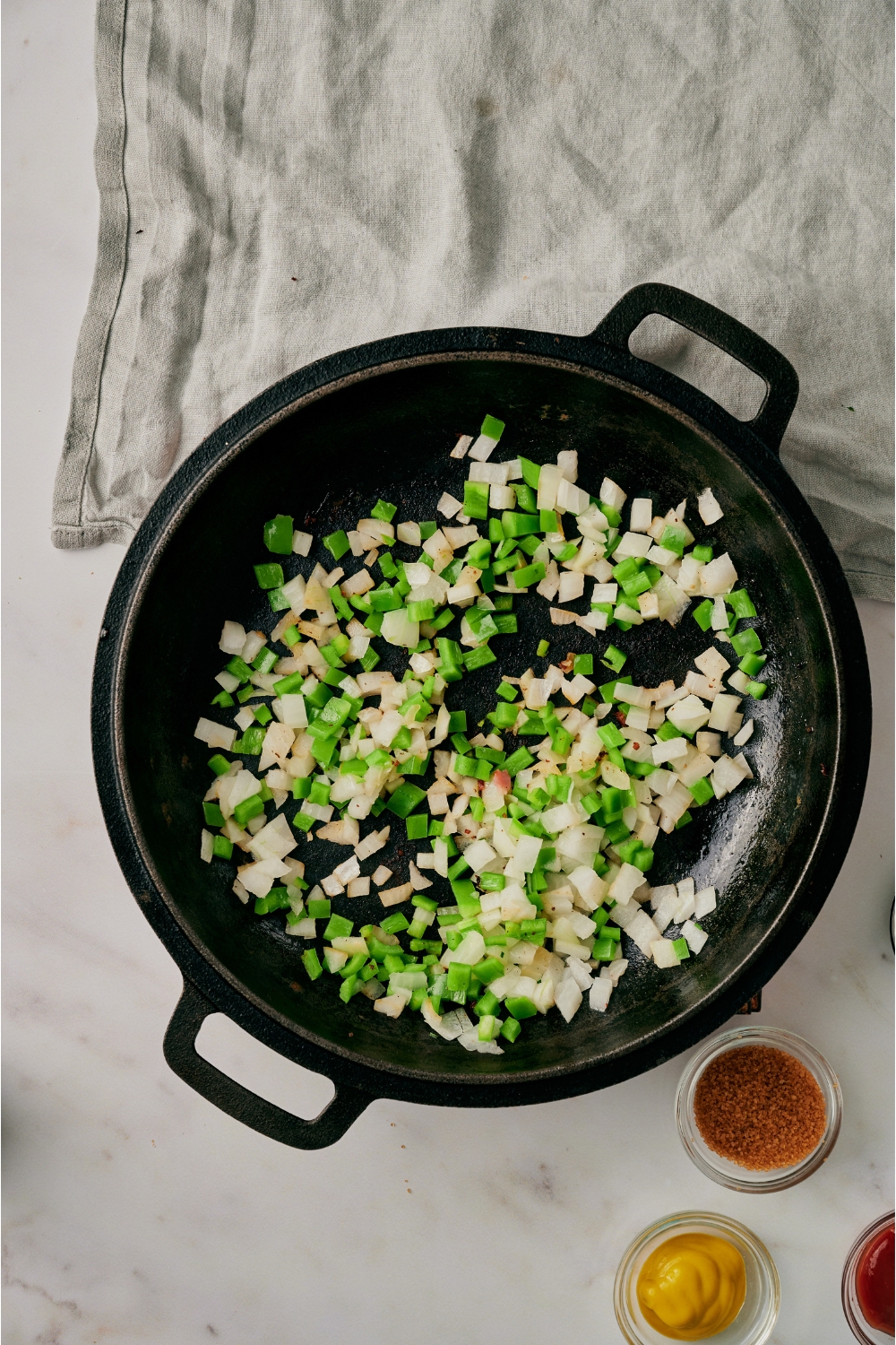 A black skillet filled with diced onion and green bell pepper.