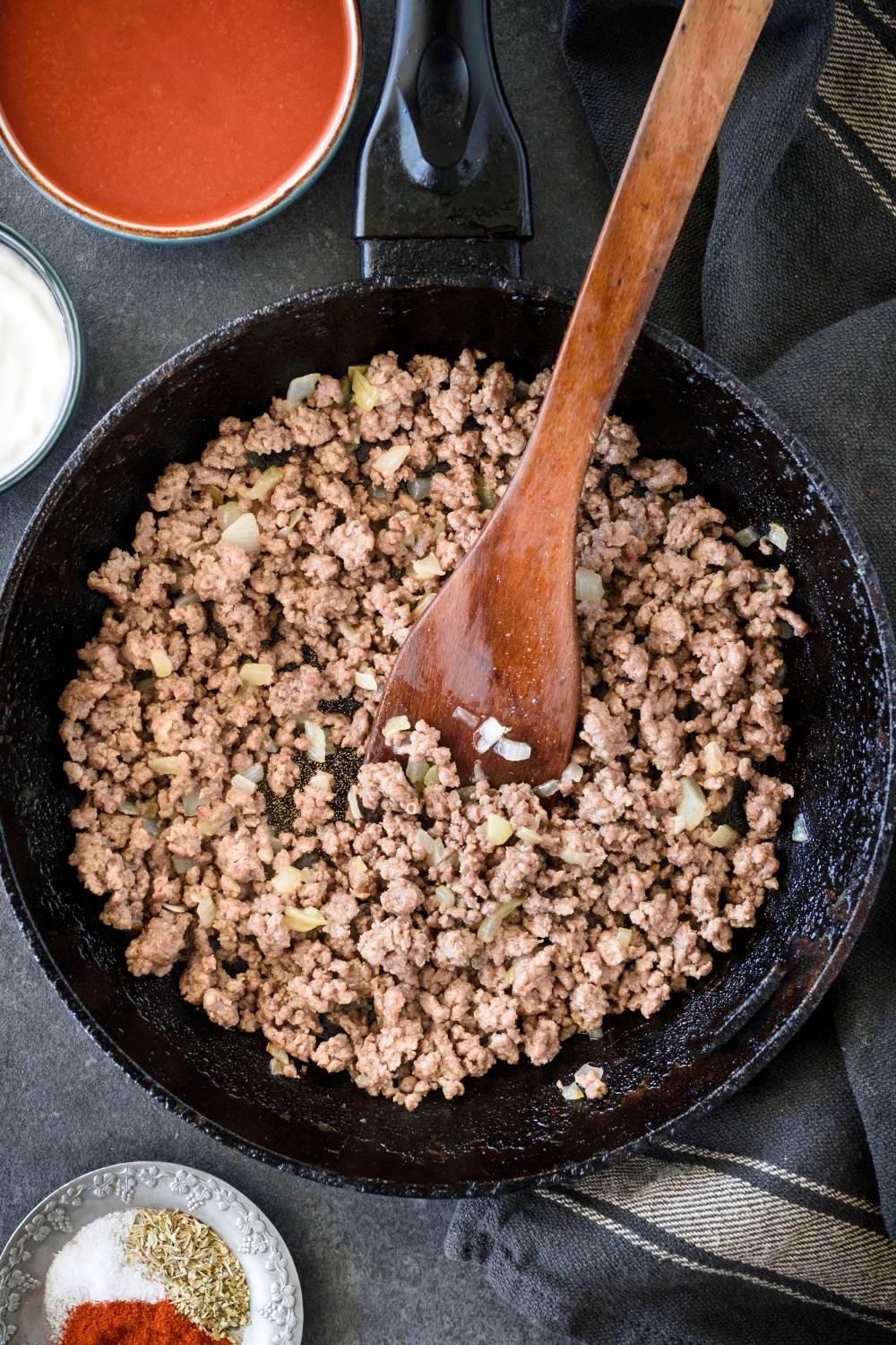 A skillet filled with diced onion and ground beef being stirred using a wooden spoon.