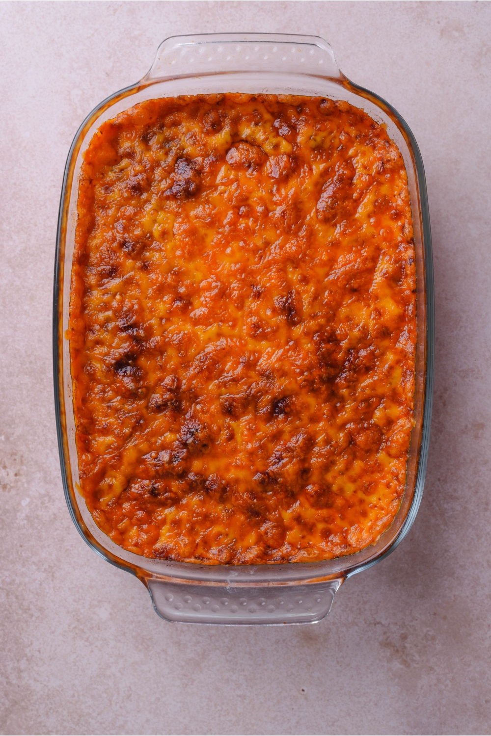 A clear baking dish filled with a freshly baked casserole topped with melted, golden brown cheese.