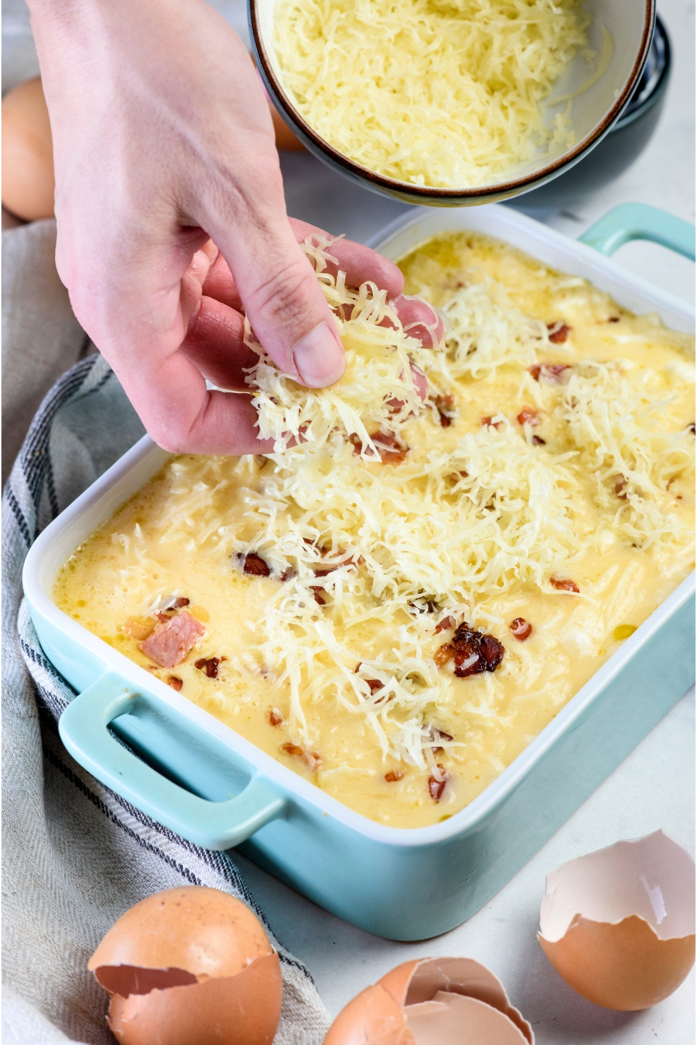 A hand spreading shredded cheese over an unbaked casserole.