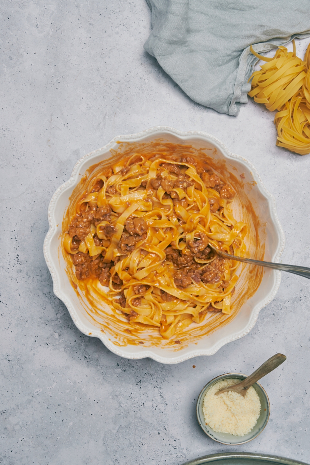 A white bowl filled with cooked noodles and ground beef in a creamy tomato sauce mixture. There is a fork in the bowl.