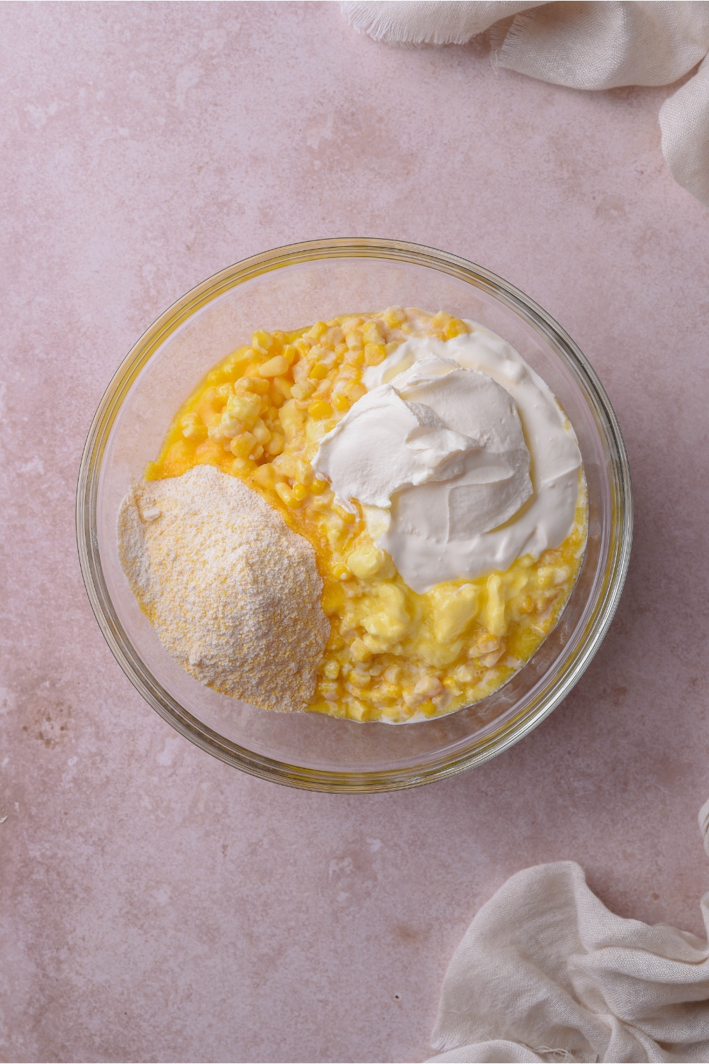 A clear bowl filled with creamed corn, sour cream, and dry muffin mix.