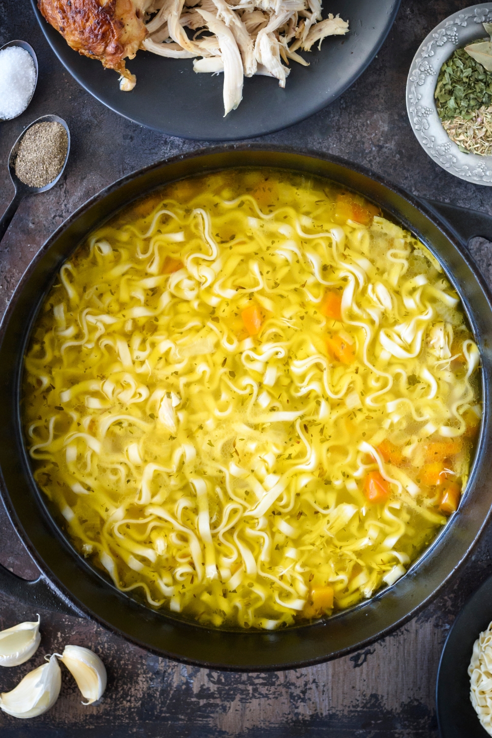 A large pot of soup with noodles and chunks of carrot floating in it.