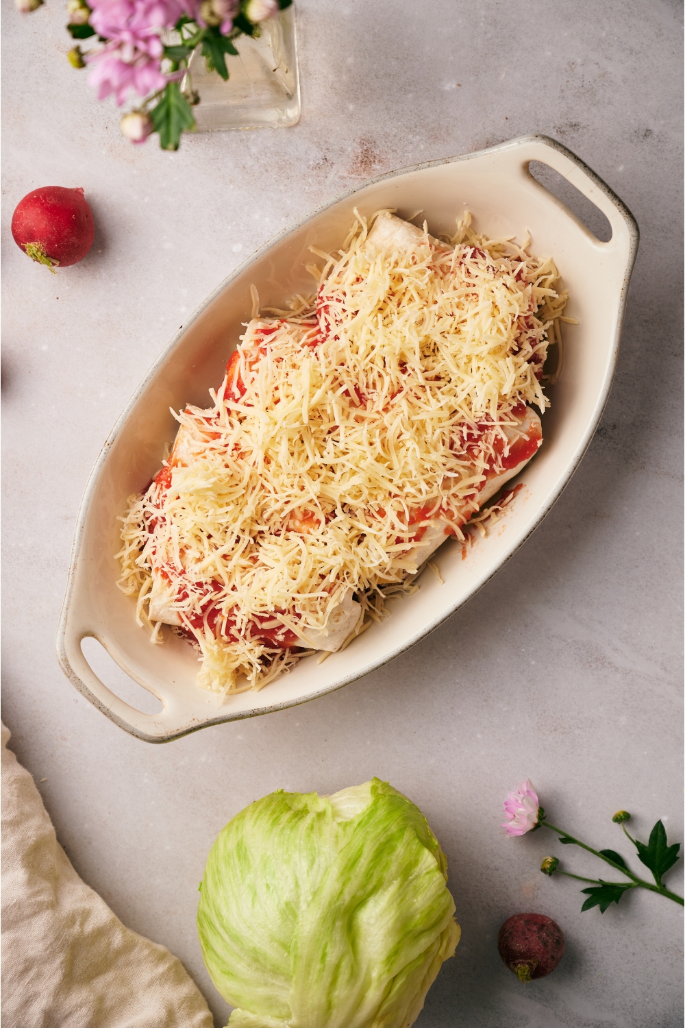 A baking dish filled with unbaked burrito casserole covered in a layer of shredded cheese.