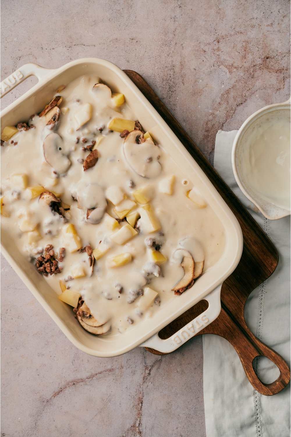 A white baking dish filled with cooked ground beef, mushrooms, and potatoes smothered in a white sauce.