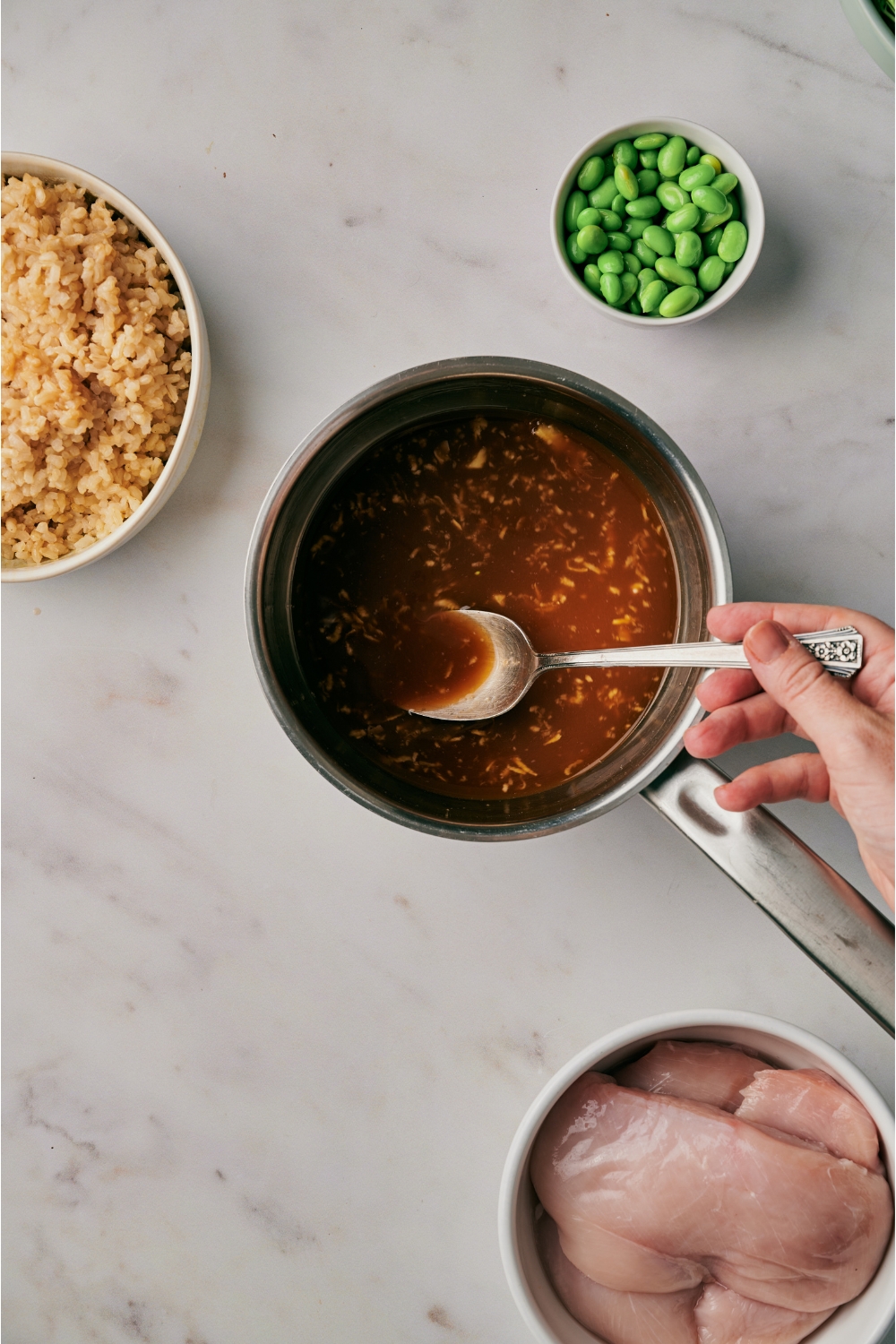 A hand stirring a pot of teriyaki sauce with a spoon.
