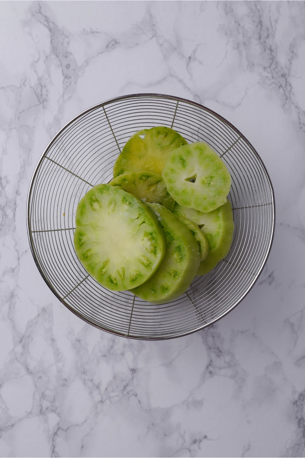 Slices of green tomatoes in a colander.