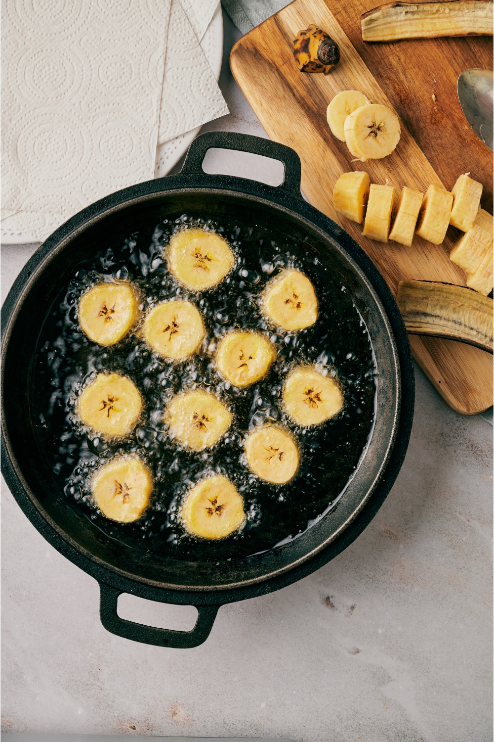 A black skillet filled with plantain slices frying in bubbling oil.
